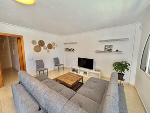 Una sala de estar moderna con sofás grises, una mesa de centro de madera, un televisor de pantalla plana, decoración en la pared y una planta en maceta.