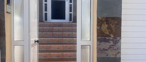 Una escalera conduce a una puerta con un panel de vidrio, rodeada de muros de piedra.