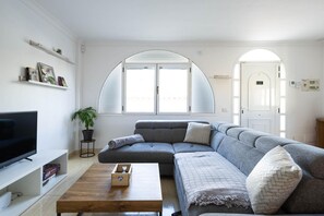 A modern living room with a sectional sofa, a flat-screen TV, a coffee table, and a potted plant.