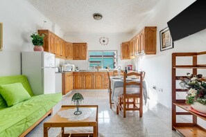 Eine moderne Küche mit Holzschränken, ein Essbereich mit Tisch und Stühlen, ein grünes Sofa und eine Uhr an der Wand.