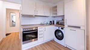 A compact kitchen with white cabinets, a built-in oven, a washing machine, and a small sink.