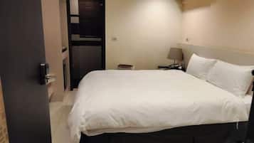 Una habitación de hotel con cama, mesita de noche, lámpara y un equipo de aire acondicionado.
