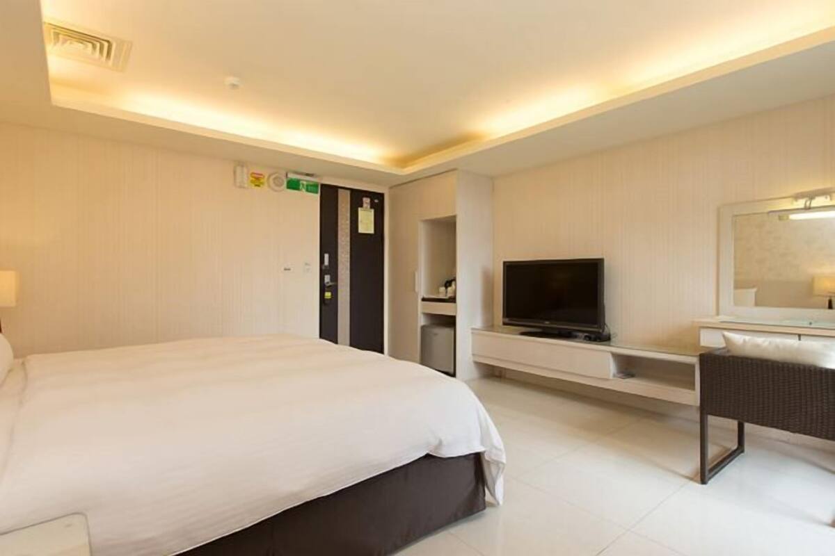 Una habitación de hotel con una cama, televisor, escritorio y espejo.