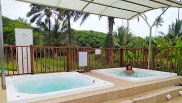 Área da piscina com duas banheiras de hidromassagem, cercada por um deck de madeira e uma grade de metal.