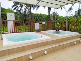 A pool area with two hot tubs, surrounded by a wooden deck and a metal fence.