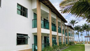 Un hotel de varios pisos con fachada blanca, amplias ventanas y un espacio al aire libre cubierto con palmeras.