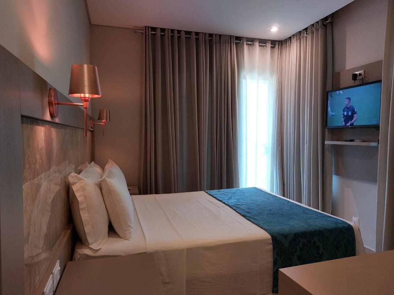 Una habitación de hotel con una cama, un televisor y cortinas.