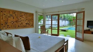 Une chambre avec un grand lit, une œuvre d’art murale en bois, une télévision et une vue sur une piscine et un jardin.