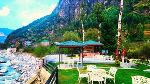 A riverside view with a gazebo, outdoor seating, and a mountain backdrop. - The Allure Grand Resort  (Manali)