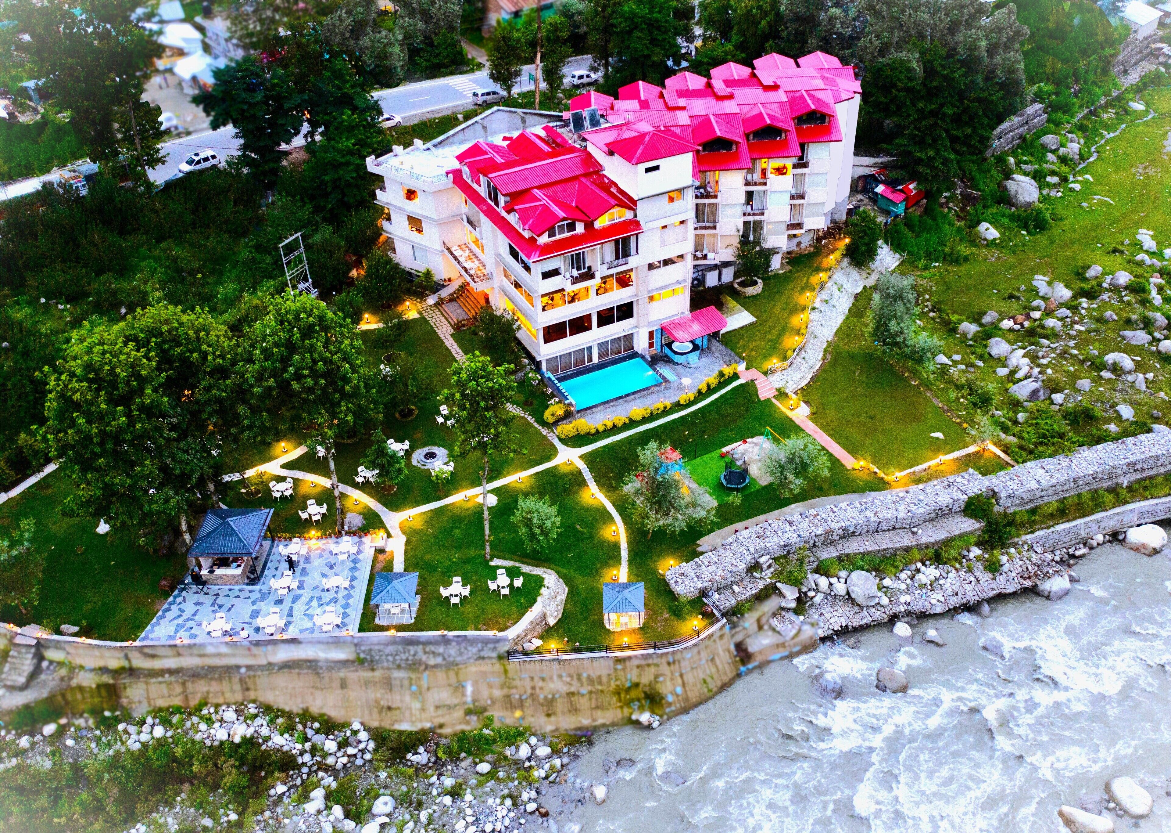Ein mehrstöckiges Hotel mit rotem Dach, umgeben von Grünflächen und einem Swimmingpool.