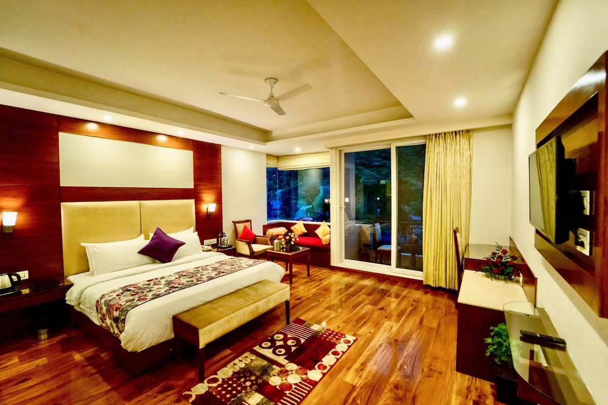 A modern hotel room with a large bed, a seating area, a TV, and a balcony with curtains.