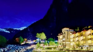 A hotel with multiple floors, a river in the foreground, and mountains in the background. - The Allure Grand Resort  (Manali)