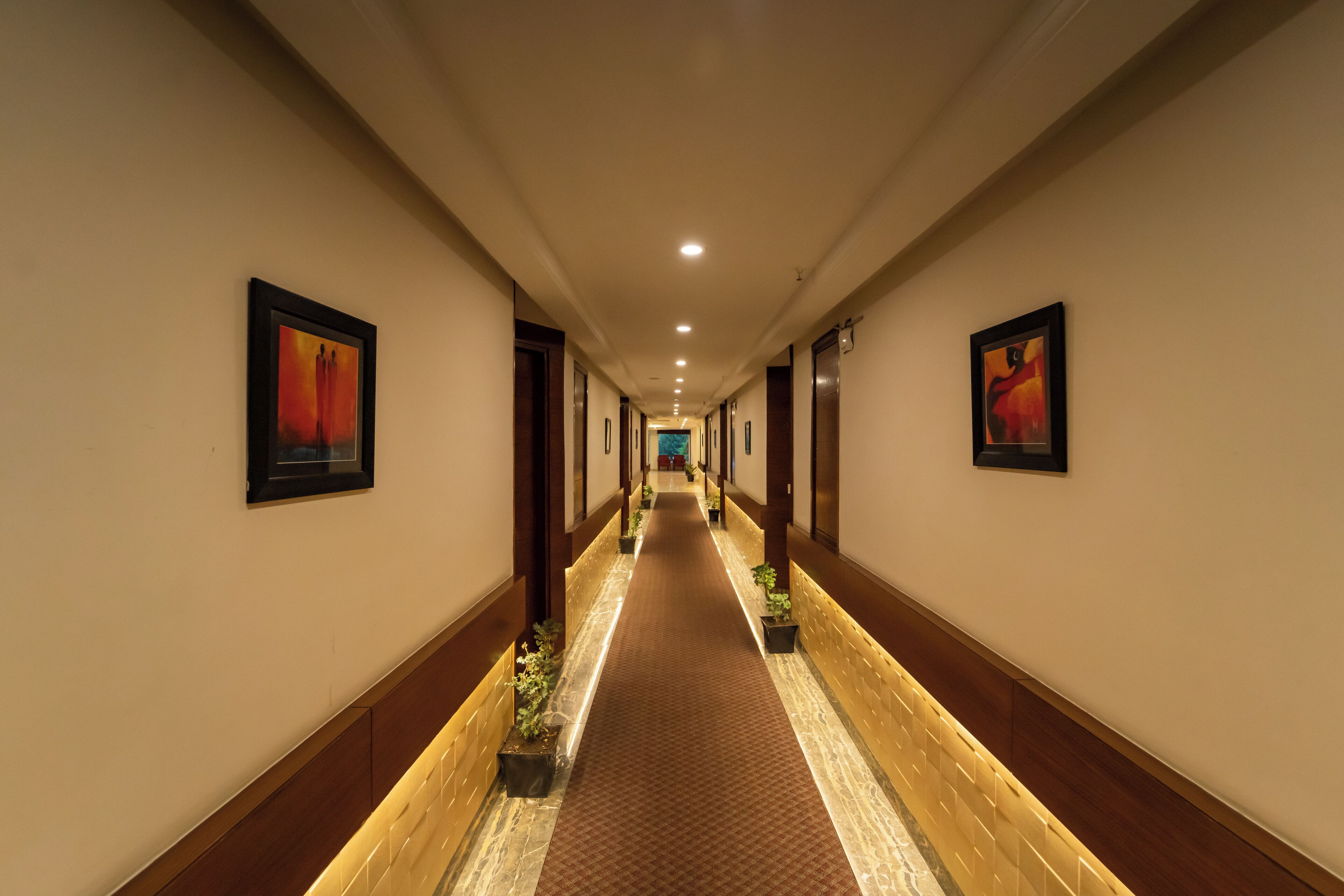 A hotel corridor with a carpeted floor, wooden paneling, and framed artwork on the walls.