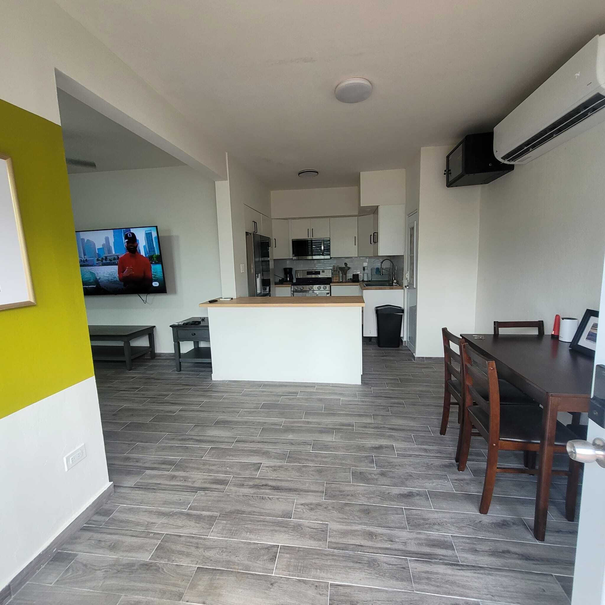 Une cuisine moderne avec des meubles blancs, un îlot central et un coin repas comprenant une table et des chaises en bois.