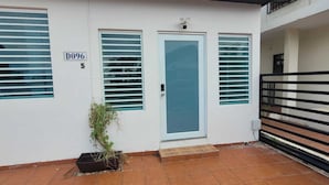 A modern building with a white facade, a blue door, and three windows with horizontal blinds. - Newly renovated 2-bed, 2-full bath condo with large pool, minutes from the beach (Carolina)