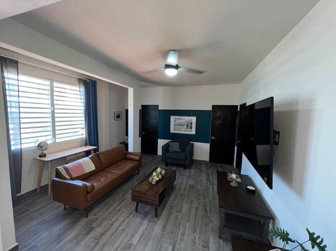 A living room with a brown sofa, a coffee table, a TV, and a ceiling fan.