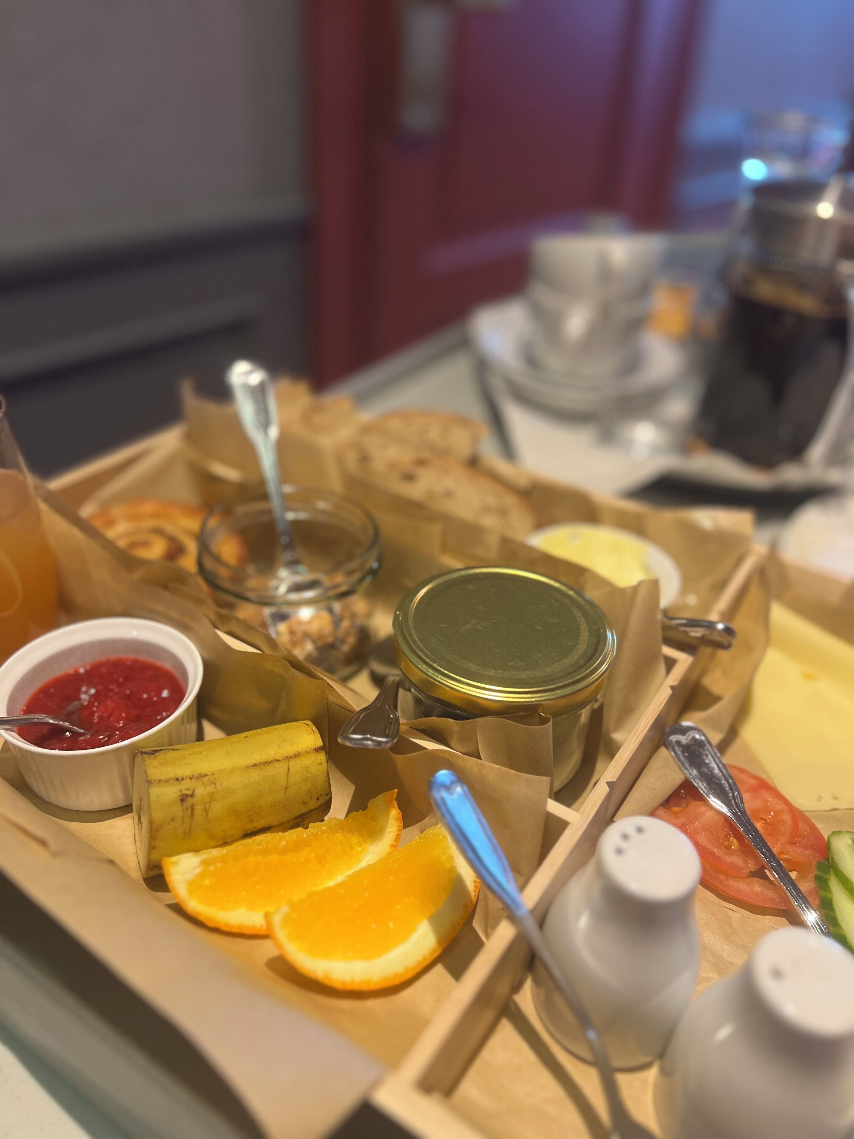 A breakfast tray with bread, butter, jam, a banana, orange slices, and condiments.