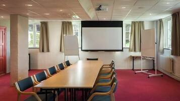 A conference room with a long table, chairs, a whiteboard, and a projector screen.