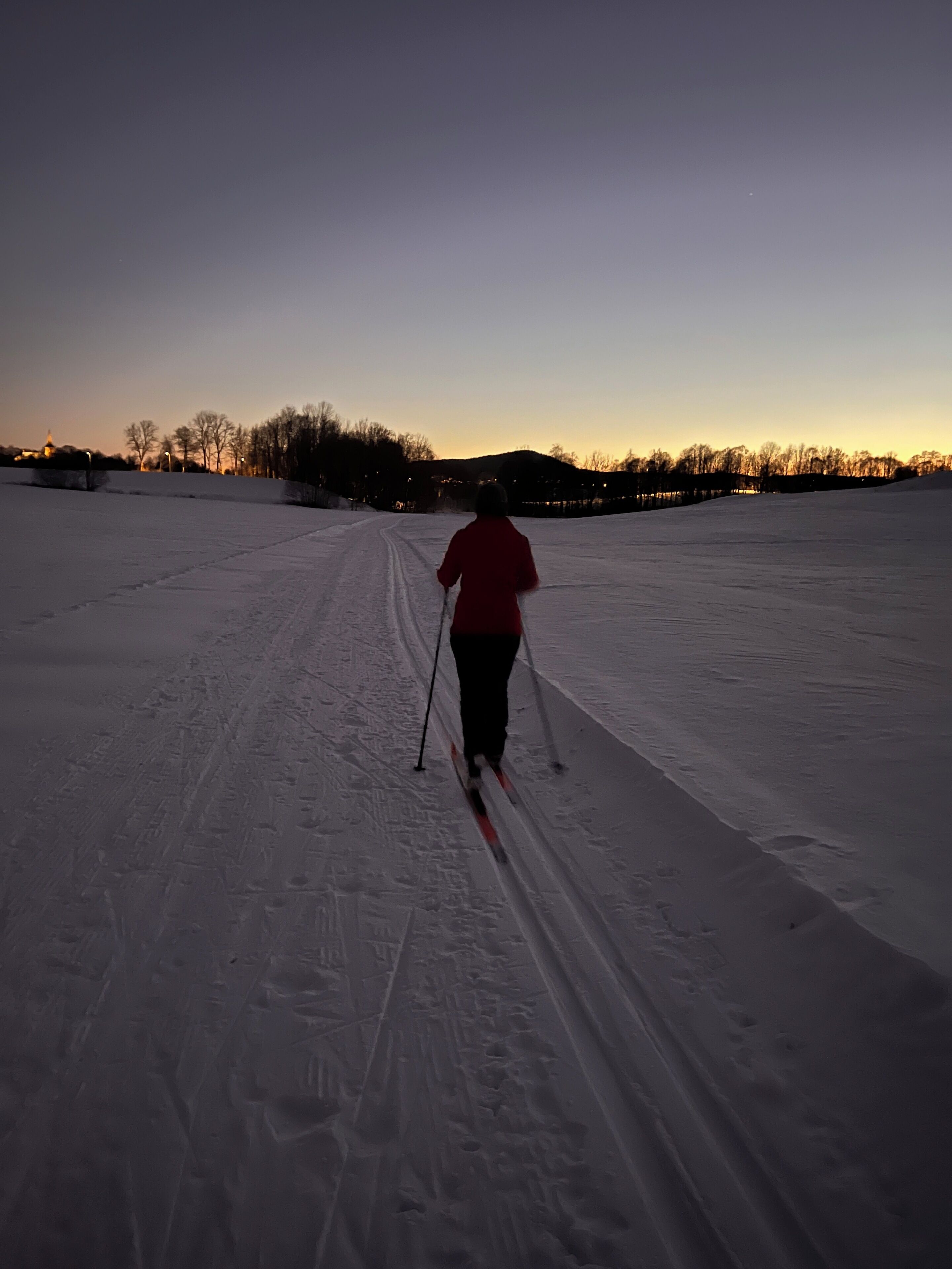 A person skiing on a snow-covered path with a sunset in the background.