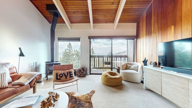 A cozy living room with a fireplace, a large TV, and a view of the outdoors. - Chic Home With Stunning Views! Modern & Natural Light, Private Washer/Dryer (Mammoth Lakes)