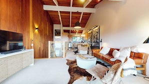 A modern living room with a large flat-screen TV, a leather sofa, and a dining area in the background. - Chic Home With Stunning Views! Modern & Natural Light, Private Washer/Dryer (Mammoth Lakes)