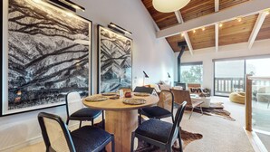 A modern dining area with a round wooden table, black cushioned chairs, and large abstract wall art. - Chic Home With Stunning Views! Modern & Natural Light, Private Washer/Dryer (Mammoth Lakes)