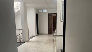 Un couloir aux murs blancs et au sol en marbre, qui mène à une porte au fond.