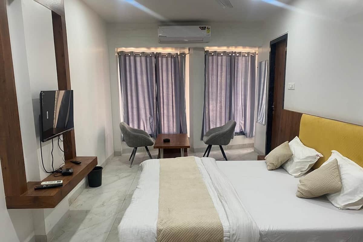 A hotel room with a bed, a TV mounted on a wooden shelf, a desk with chairs, and curtains.