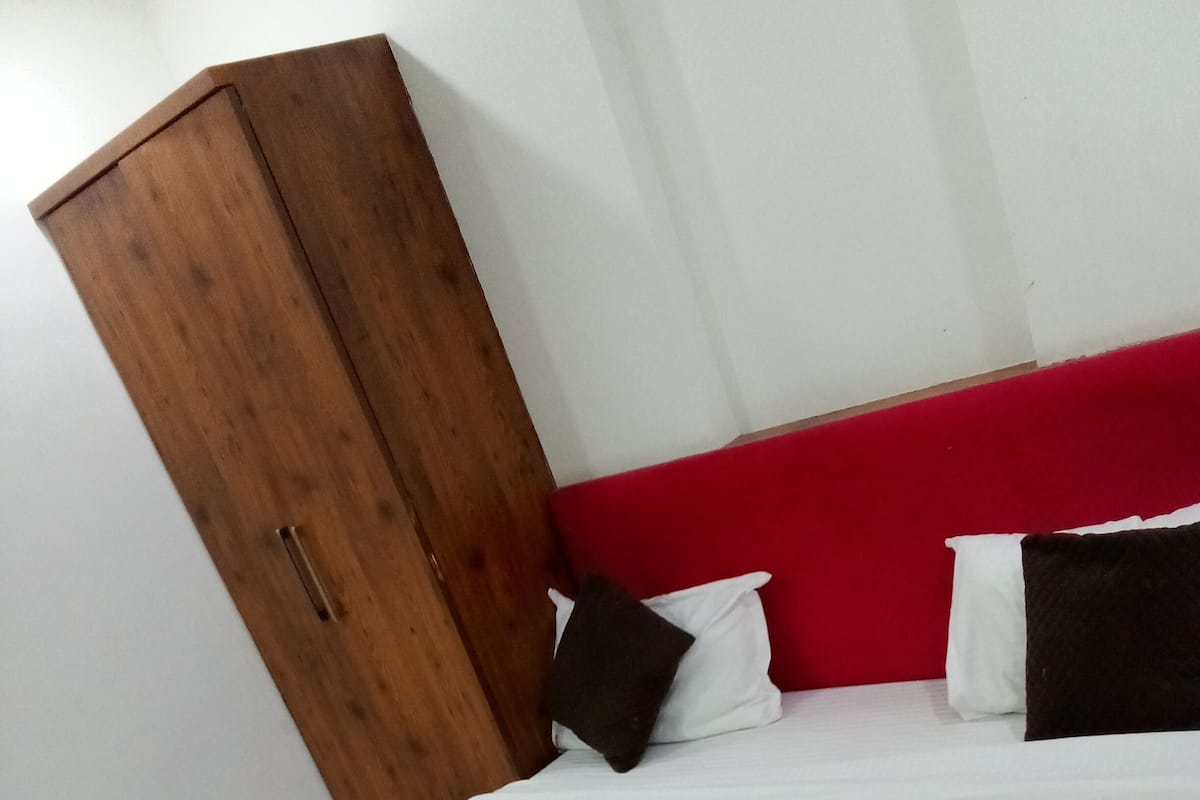 A bed with white and brown bedding, a red headboard, and a wooden wardrobe.