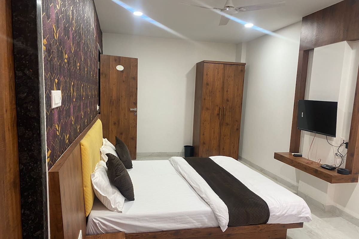 A bedroom with a bed, wooden wardrobe, a TV mounted on the wall, and a ceiling fan.
