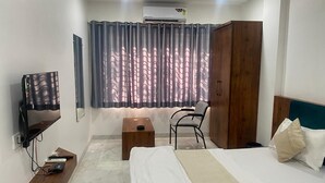 Une chambre d’hôtel avec un lit, une chaise, une télévision, une armoire et une fenêtre avec des rideaux.