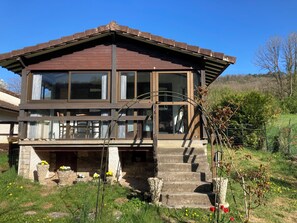 Een huis met twee verdiepingen, een stenen fundering, grote ramen en een houten terras.