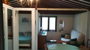 A cozy room with a bed, a dining table with chairs, a small kitchen area, and a window with curtains. - Chalet at the end of the world.    (Cormot-Vauchignon)