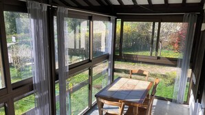 A covered patio with a table and chairs, large windows, and a view of a garden. - Chalet at the end of the world.    (Cormot-Vauchignon)