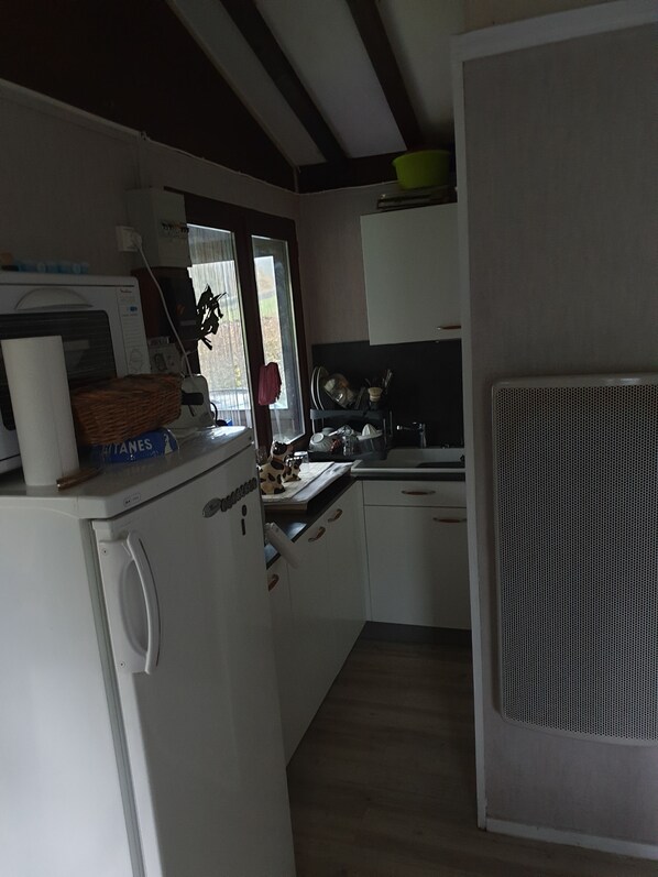 Een compact keuken met een koelkast, magnetron en een raam met uitzicht op groen.