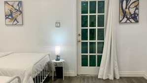 Ein Schlafzimmer mit Bett, Nachttisch, Lampe und einer Tür mit Vorhängen.