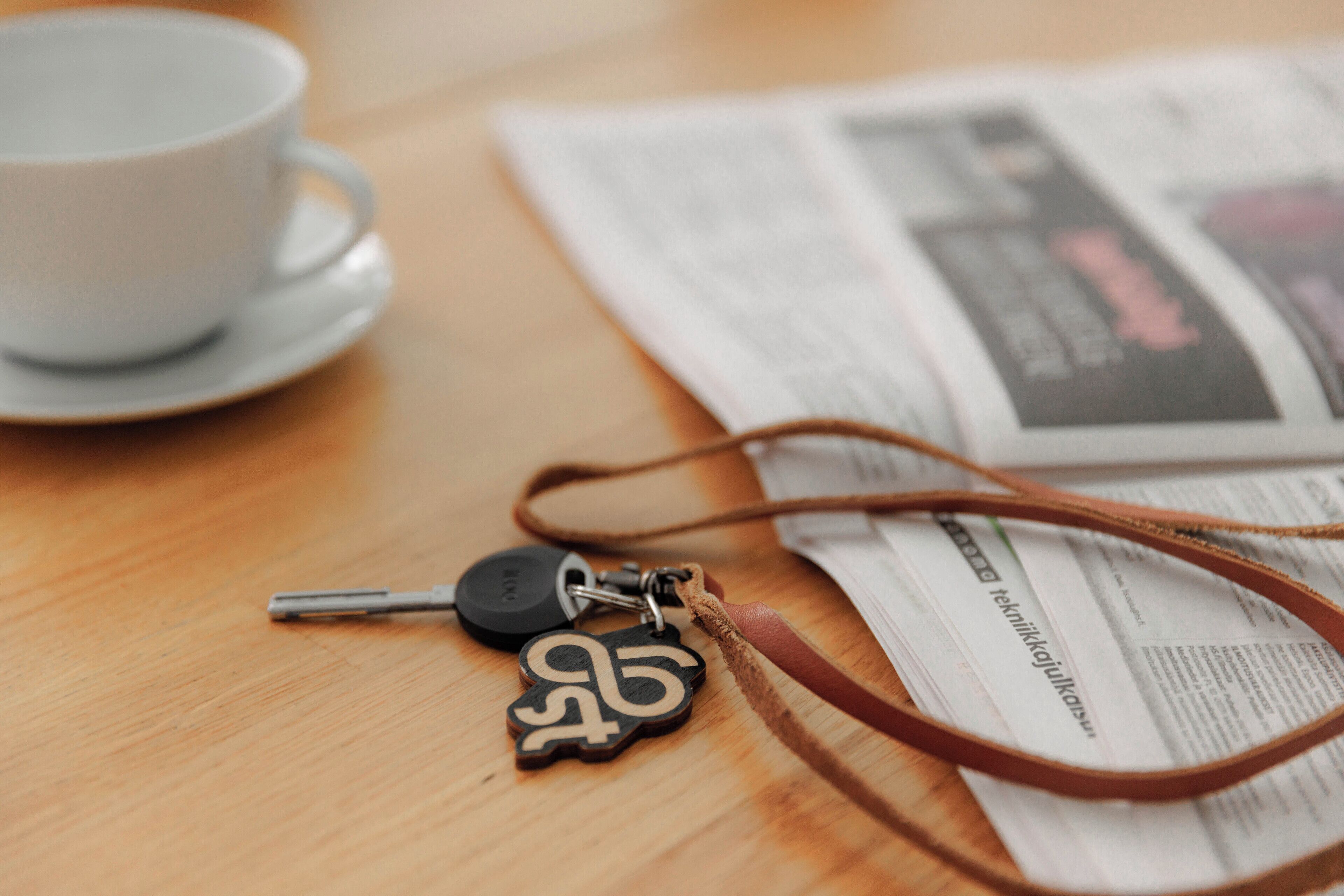 A wooden table with a white cup, a newspaper, and a keychain.