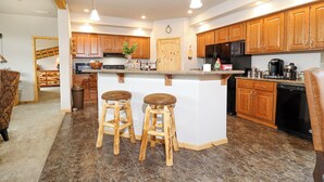 A modern kitchen with wooden cabinets, a central island with stools, a refrigerator, and a coffee maker.