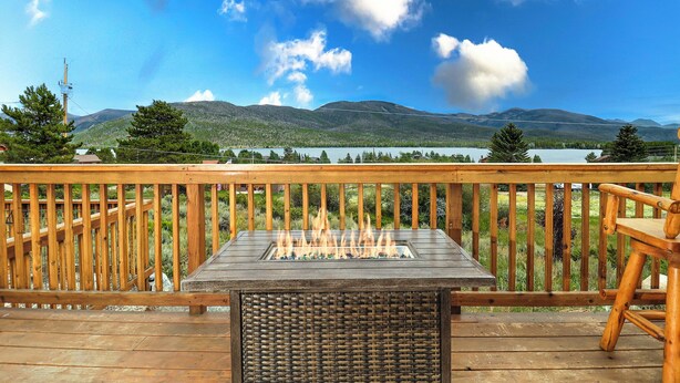 A deck with a fire feature, wooden railings, and a view of mountains and a lake.