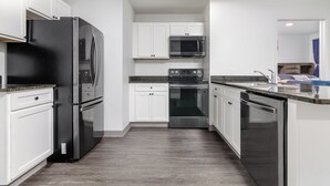 Una cocina moderna con gabinetes blancos, electrodomésticos de acero inoxidable y una encimera de granito.