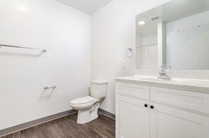Ein modernes Badezimmer mit Toilette in Weiß, einem Waschtisch mit Spiegel und Holzboden.