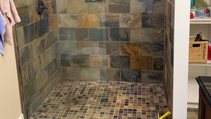 Zona de ducha con azulejos de piedra, ducha de mano y cabina de ducha con mampara de vidrio.