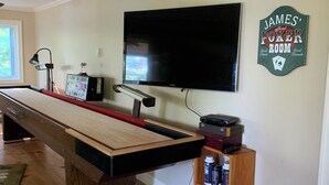 Una mesa de billar con un televisor montado encima, un pequeño estante con bebidas y un cartel en la pared.