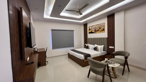 A modern hotel room with a large bed, a desk, a chair, and a small table. - Hotel Sun Flowers (Alwar)