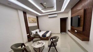 A modern living room with a sofa, two armchairs, a coffee table, a ceiling fan, and a flat-screen TV mounted on the wall. - Hotel Sun Flowers (Alwar)