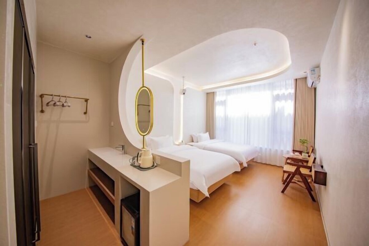 A hotel room with a bed, a desk with a mirror, a small table, and a chair.