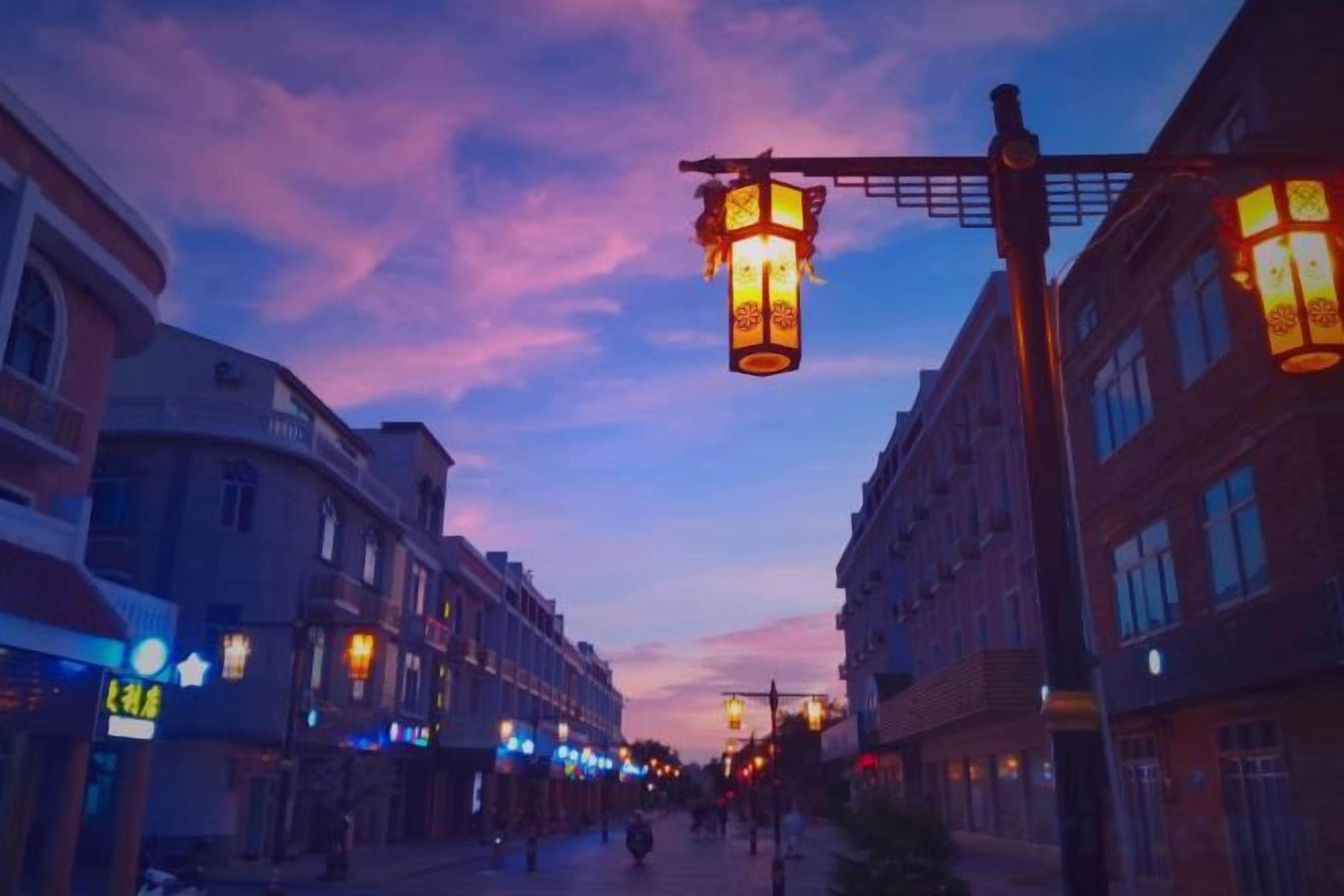 A street at dusk with illuminated street lamps and buildings.