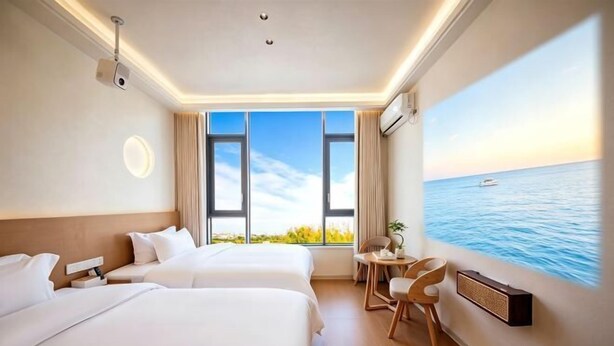 Une chambre d’hôtel avec deux lits, un bureau, une chaise, une grande fenêtre donnant sur la mer et un tableau représentant la mer accroché au mur.