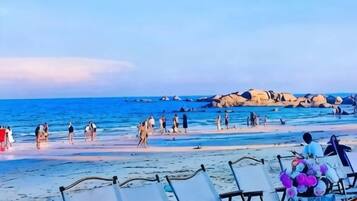 A beach with rows of empty lounge chairs and a rocky shoreline in the background.