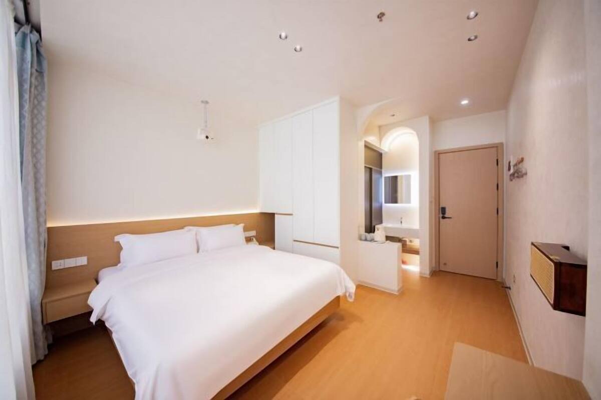 Une chambre d’hôtel avec un grand lit, un dressing, une salle de bain avec un miroir et un plancher en bois.